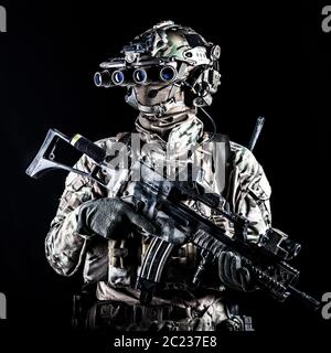 Marine rider in camouflage uniform and face mask, patrolling in darkness with quad-tube night vision goggles on battle helmet, holding modern assault Stock Photo