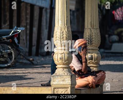 Somnath, Gujarat, India - December 2018:  Portrait of a young Indian monk sitting inside an old temple and talking on the phone. Stock Photo