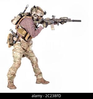 Full length portrait of airsoft player in checkered shirt, wearing camouflage uniform, helmet with tactical radio headset, body armour, aiming with se Stock Photo