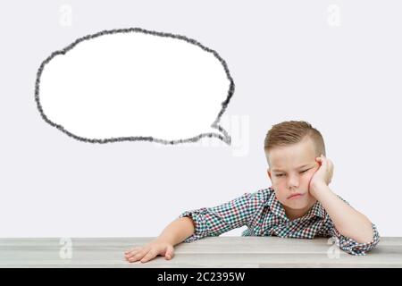 Caucasian school-age boy in a plaid shirt falls asleep sitting at the table Stock Photo