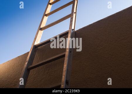 Low angle view of metal ladder leaning against concrete wall, the background is a clear sky. Conceptual themes of overcoming obstacles, challenges and Stock Photo