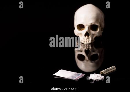 cocaine, Herion or other illegal drugs that are sniffed by means of a tube or injected with a syringe, money and Skull, isolated on black glossy backg Stock Photo