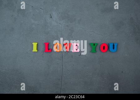 The multicolored I love you word is made of wooden letters on a grey plastered wall background Stock Photo