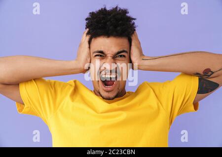 Photo of displeased african american man covering his ears and screaming isolated over purple background Stock Photo