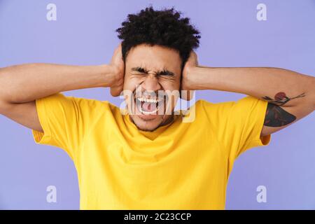 Photo of displeased african american man covering his ears and screaming isolated over purple background Stock Photo