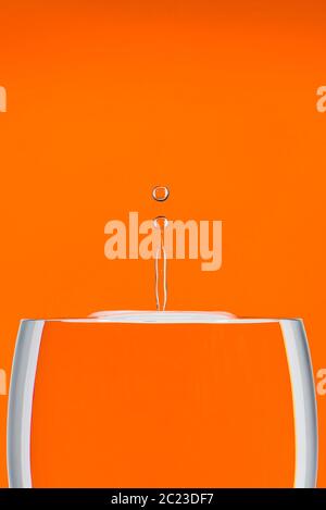 Indoor studio image of a high-speed falling water drop against an orange background Stock Photo