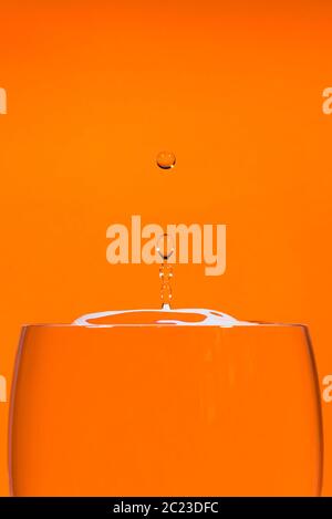 Indoor studio image of a high-speed falling water drop against an orange background Stock Photo