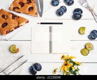 open notebook with blank white pages, baked pie with plums and fresh fruits, top viewflat lay Stock Photo