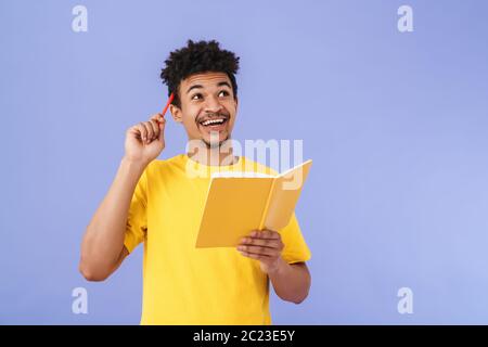 Photo of excited african american man smiling and making notes in planner isolated over purple background Stock Photo