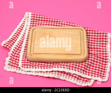 small kitchen wooden cutting board and white red checkered kitchen towel on a pink background, bright picnic background, copy space Stock Photo