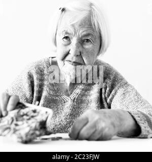 Concerned elderly 96 years old woman sitting at table at home and counting remaining coins from pension in her wallet after paying bills. Unsustainabi Stock Photo