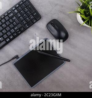 Working place on dark table with copy space. Keyboard, computer mouse, pen, graphics tablet, flower in pot. Flat lay. Stock Photo