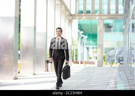 Businessman with suitcase walking outside office building. Stock Photo