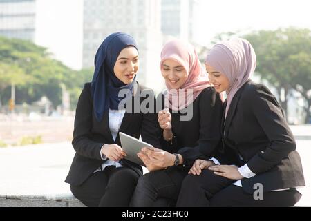 Group of Muslim business women discussing, using tablet pc outdoor. Stock Photo