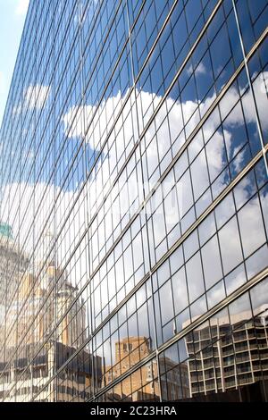 Old and modern buildings and a very blue sky with towering white fluffy clouds are reflected in the side of a tall glass building Stock Photo