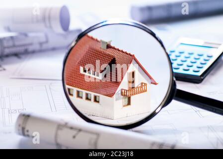 House under a magnifier with building plans and calculator Stock Photo