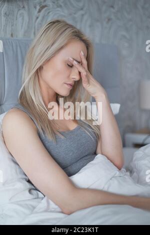 Women sitting on bed holding her head. She has a painful headache Stock Photo