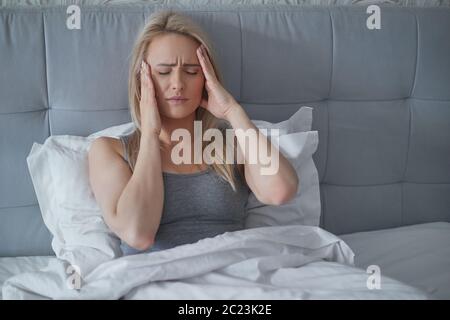 Women sitting on bed holding her head. She has a painful headache Stock Photo