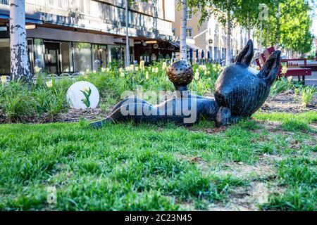 UMEA, SWEDEN - JUNE 10, 2020: Bronze sculpture of cat laying on back and playing with ball, closeup photo of brown kitten on green grass under birches Stock Photo