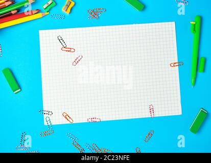 white squared paper from notebooks, wooden colored pencils, paper clips on a blue background, back to school Stock Photo