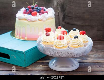 Pink cake with melted chocolate, strawberry, blueberry and cherry and cupcakes with whipped cream and fresh berries. Stock Photo