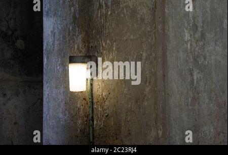 Single lamp shining on dark dirty concrete wall. Stock Photo