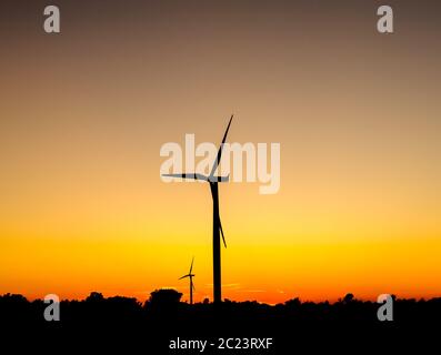 Black silhouette of wind turbines against orange sky at dusk. Stock Photo