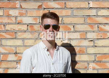Smiling young man portrait with retro shiny drop sunglasses against brick wall Stock Photo