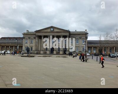 Huddersfield, West Yorkshire, England - April 26, 2018: Pedestrians in St Georges Square walk past the historic railway station