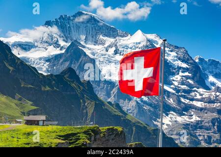 Swiss flag wavingon a Mannlichen viewpoint with peak of Jungfrau mountain on the background, Bernese Oberland Switzerland Stock Photo