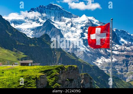 Swiss flag wavingon a Mannlichen viewpoint with peak of Jungfrau mountain on the background, Bernese Oberland Switzerland Stock Photo