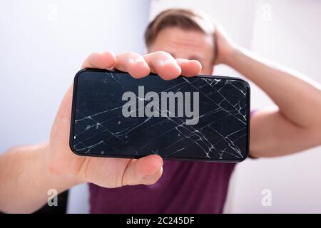 Worried Man Holding Broken Smartphone At Home Stock Photo