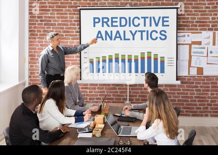 Businessman Giving Predictive Analytics Presentation To His Colleagues In Office Stock Photo