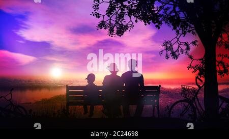 Silhouettes of family with a child sitting on a park bench and watching sunset over the river. Stock Photo