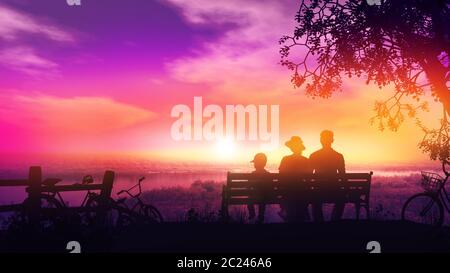Silhouettes of family sitting on a park bench and watching sunset after a bike ride. Stock Photo