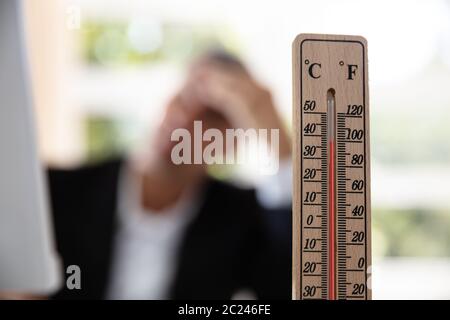 Thermometer In Front Of Businessman Working During Hot Weather In The Office Stock Photo