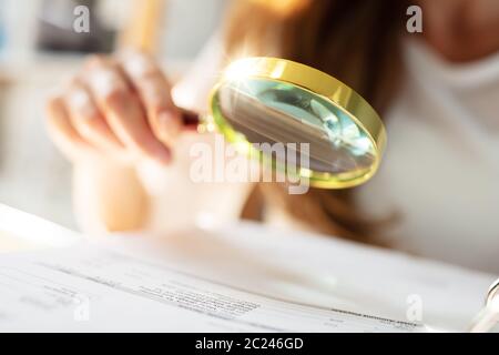 Businessperson Analyzing Bill Through Magnifying Glass In Office Stock Photo