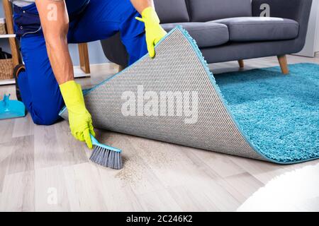 Low section View Of A Lazy Janitor Sweeping Dirt Under The Carpet Stock Photo