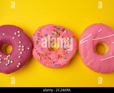 three round different sweet donuts with sprinkles on a yellow background, top view Stock Photo