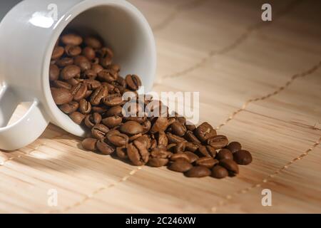 Coffee beans are poured from a white Cup lying on the table Stock Photo