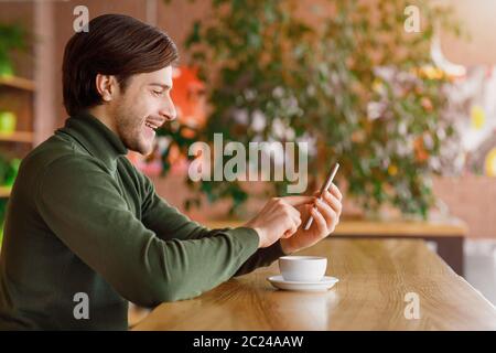 Young man using smartphone while drinking coffee at cafe Stock Photo