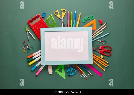 Blue frame with blank sheet and stationery accessories: pencils, pens, other office supplies on green background. Top view, copy space.  School access Stock Photo