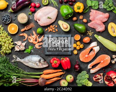 Pegan diet conept. Vegan plus paleo diet food ingredients - vegetables, fruits, raw meat and fish on dark background. Top view or flat lay Stock Photo