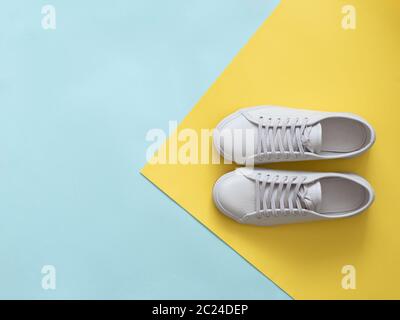 White leather sneakers on blue and yellow background. Pair of fashion trendy white sport shoes or sneakers with copy space for text on colorful backgr Stock Photo