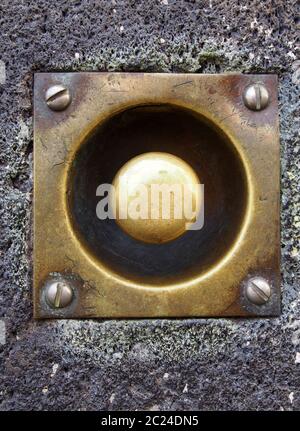 a close up of an old tarnished doorbell button with screws in a grey house wall Stock Photo