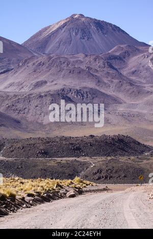 Dirt road leads with serpentines on high mountain in front of volcano Stock Photo