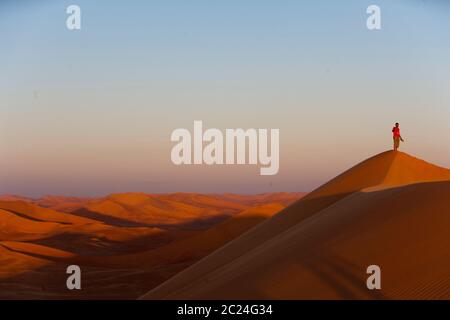 An office worker at a oil facility being developed in the Sahara desert, North Africa, walks  a high dune in the late afternoon. Stock Photo