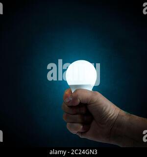 a light bulb on in hand with an antique blue background Stock Photo