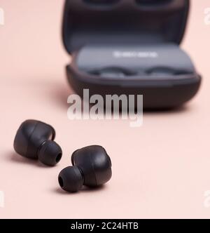 black wireless little earphones and a charging box on a beige  background Stock Photo