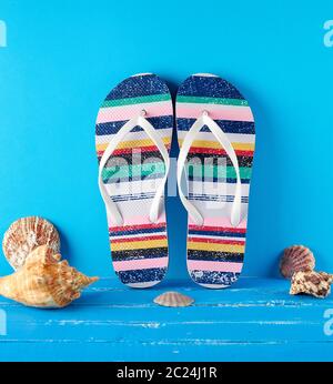 pair of multi-colored rubber slippers on a blue background, near seashells, background for travel and leisure Stock Photo